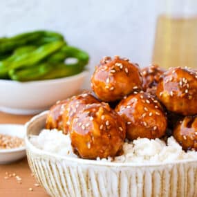 Baked chicken teriyaki meatballs on top of a bowl white rice and sprinkled with sesame seeds.