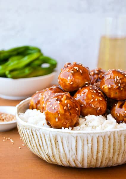 Baked chicken teriyaki meatballs on top of a bowl white rice and sprinkled with sesame seeds.