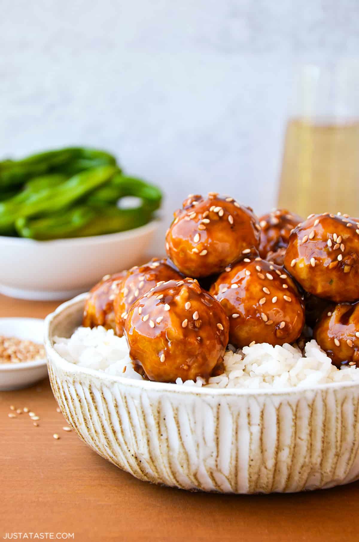 A dinner bowl containing baked chicken teriyaki meatballs on top of white rice and sprinkled with sesame seeds.