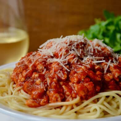 A bowl of spaghetti topped with turkey bolognese and grated cheese.