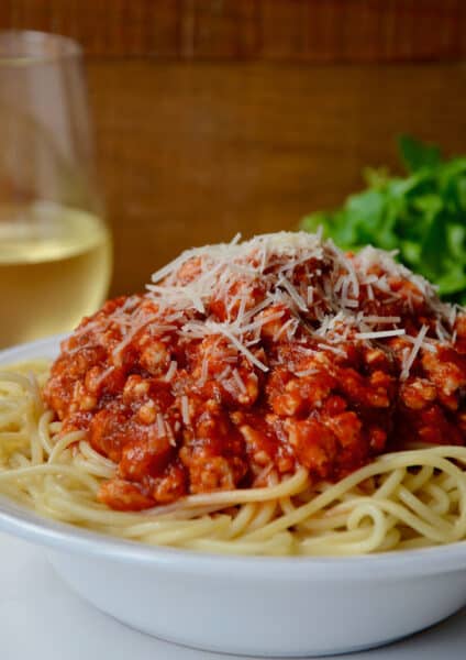 A bowl of spaghetti topped with turkey bolognese and grated cheese.