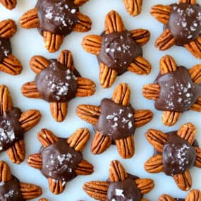 Chocolate turtles topped with flakey salt on a parchment-lined baking sheet.