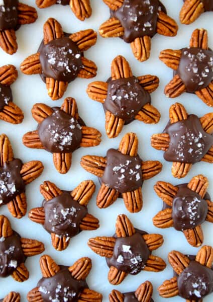 Chocolate turtles topped with flakey salt on a parchment-lined baking sheet.