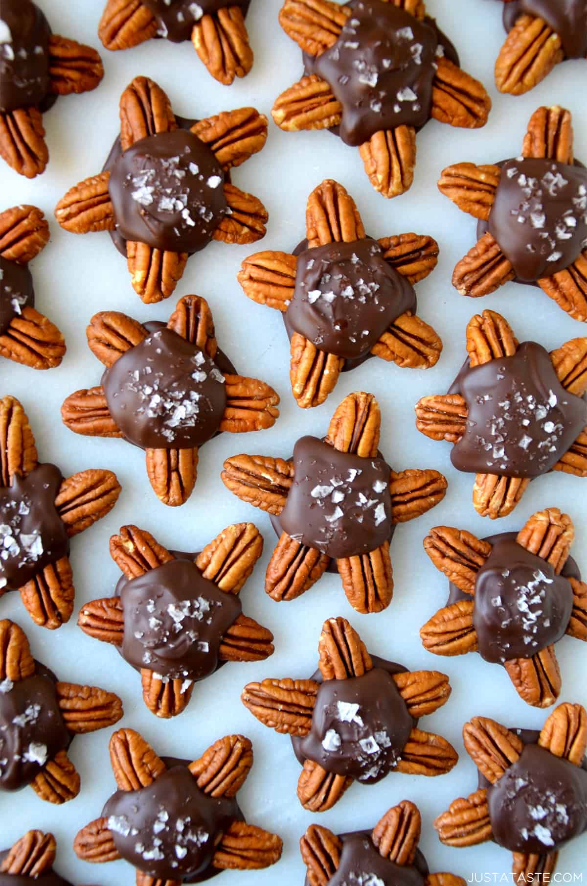 Chocolate turtles topped with flakey salt on a parchment-lined baking sheet.