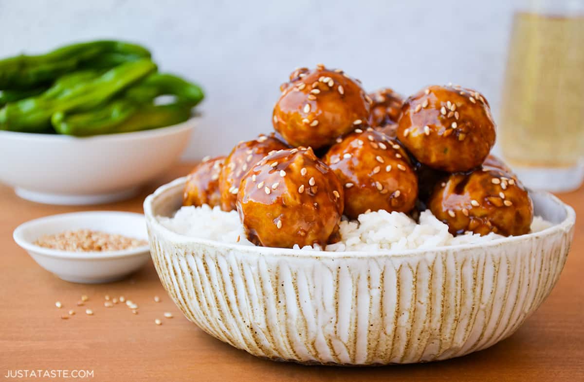 A bowl with white rice and chicken teriyaki meatballs with sesame seeds sprinkled on top.