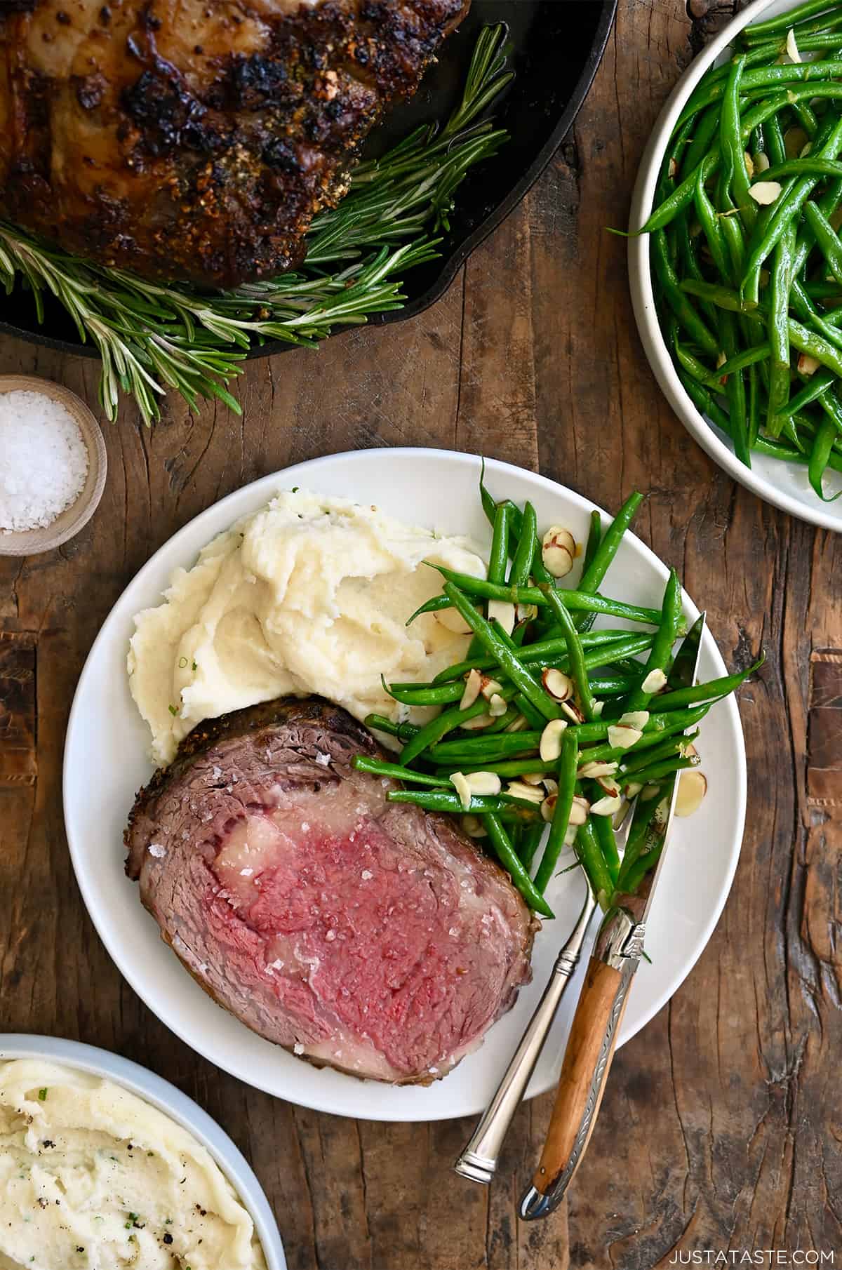 Prime rib cooked to medium-rare on a dinner plate with blistered green beans and mashed potatoes. 