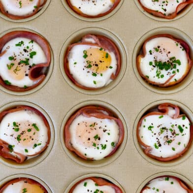 Baked ham and egg cups garnished with fresh chives in a muffin tin.