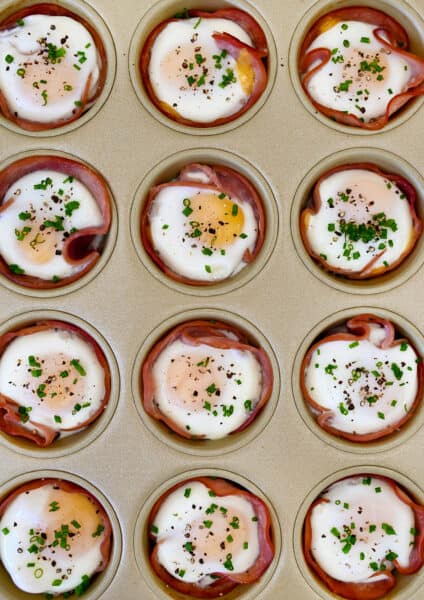 Baked ham and egg cups garnished with fresh chives in a muffin tin.