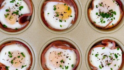 Baked ham and egg cups garnished with fresh chives in a muffin tin.