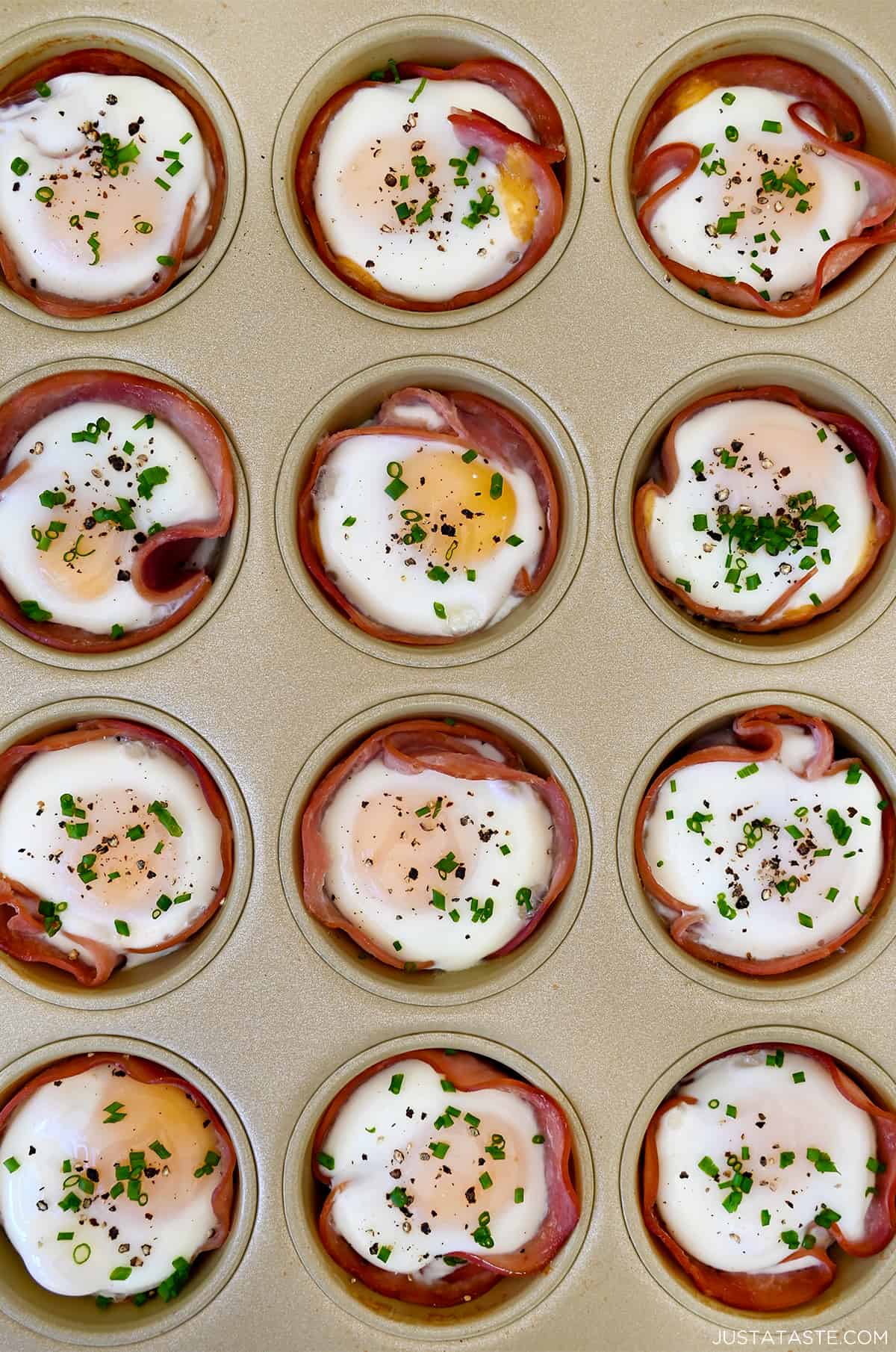 Baked ham and egg cups garnished with fresh chives in a muffin tin.