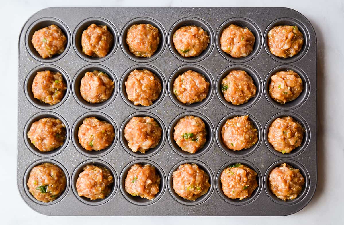 Unbaked chicken meatballs in a greased mini muffin tin.