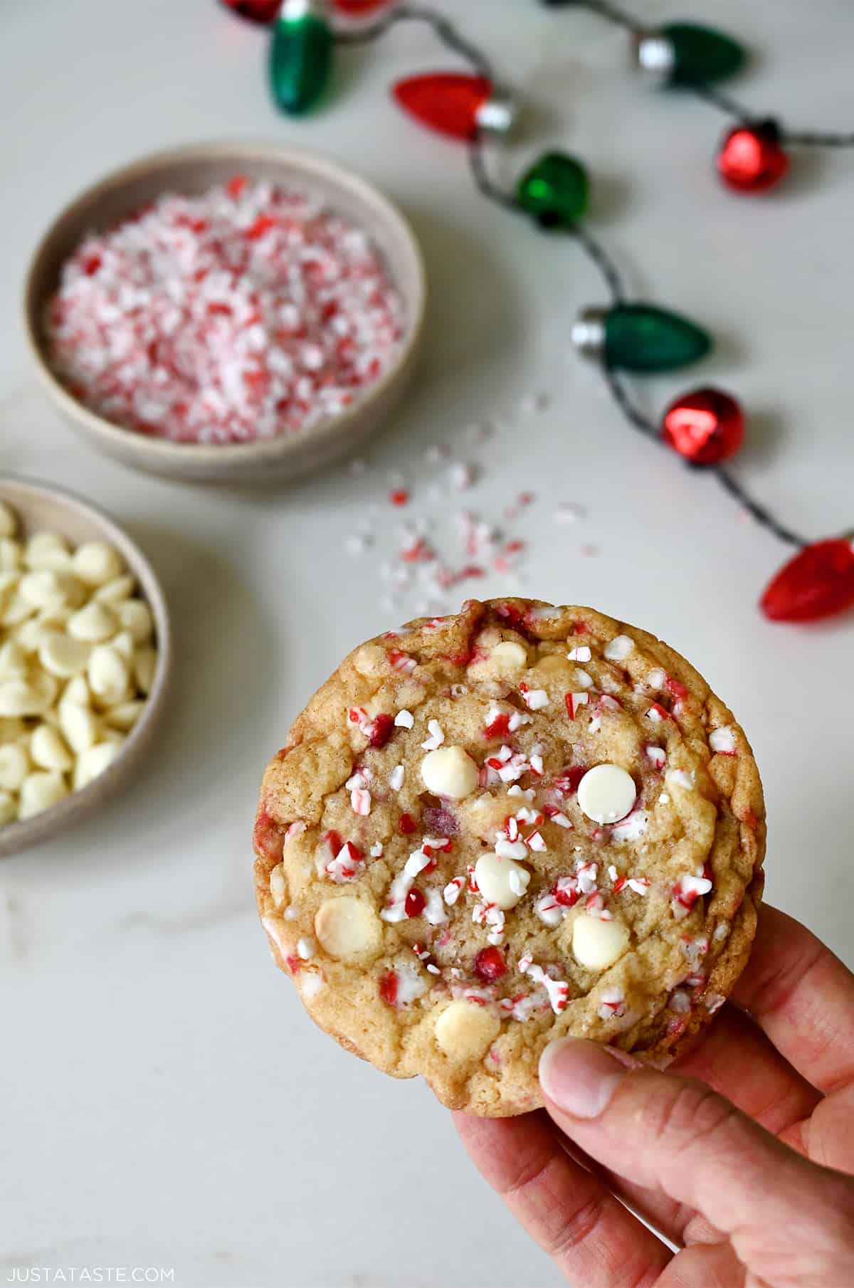 A hand holds a cookie that's studded with white chocolate chips and crushed candy canes.