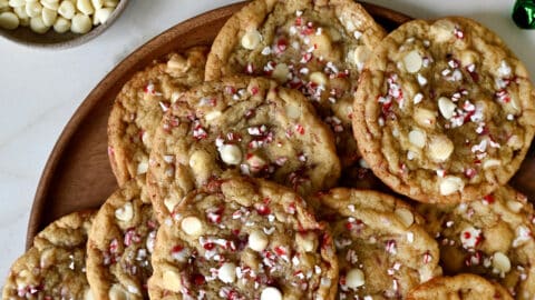 White chocolate peppermint cookies on a platter next to a two small bowls containing white chocolate chips and crushed candy canes.