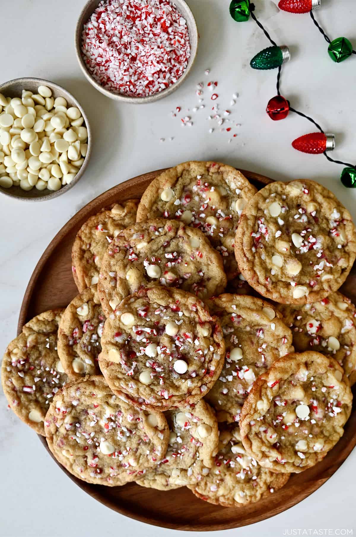 White chocolate peppermint cookies on a platter next to a two small bowls containing white chocolate chips and crushed candy canes.