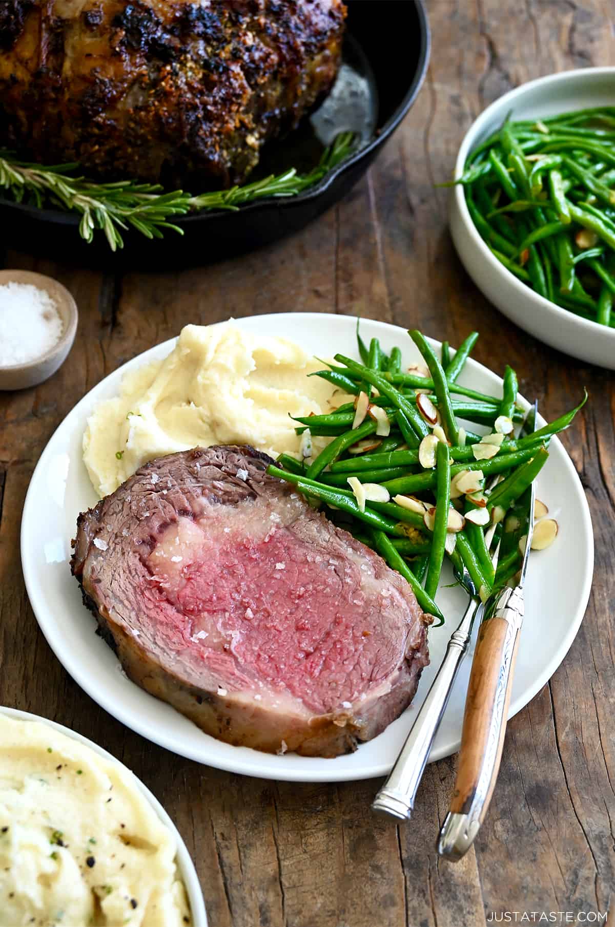 Medium-rare prime rib on a white dinner plate with green beans and mashed potatoes. A fork and knife are also on the plate.