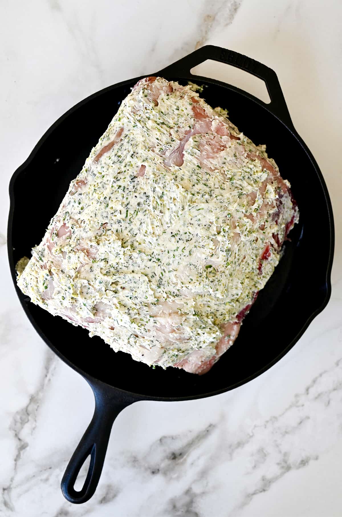 Rib roast coated in a garlic-herb butter rub in a cast-iron skillet.