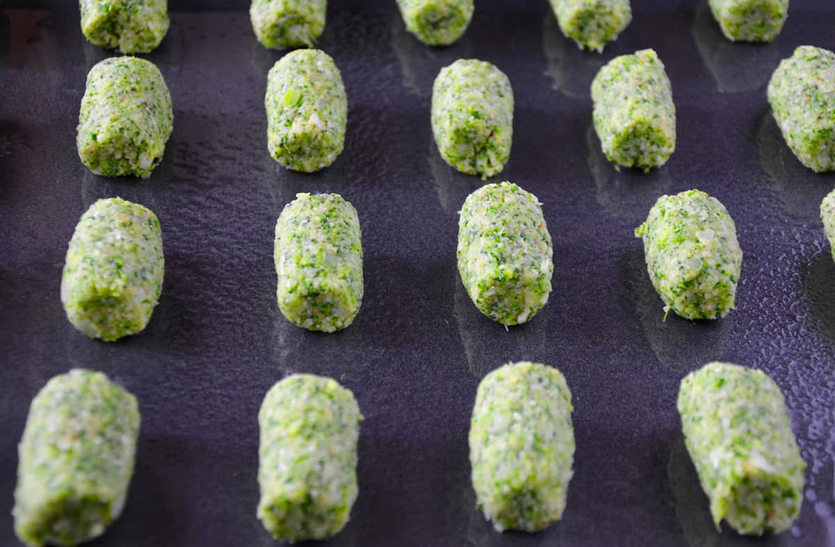 Unbaked broccoli tots on a greased nonstick baking sheet.