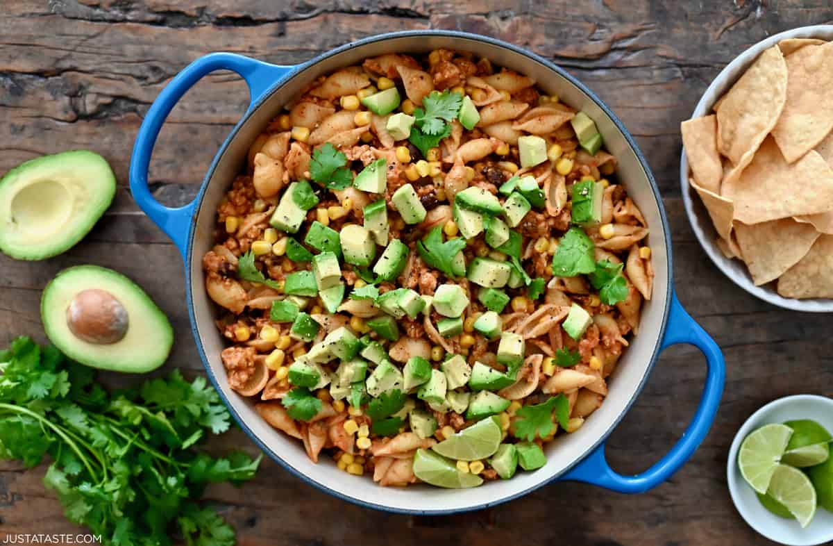 A large Dutch oven containing cheesy taco pasta shells topped with diced avocado and cilantro.