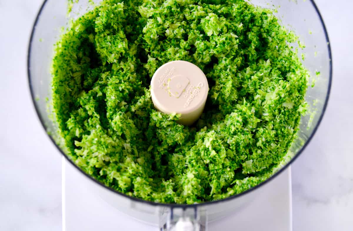 Finely ground broccoli in the bowl of a food processor.