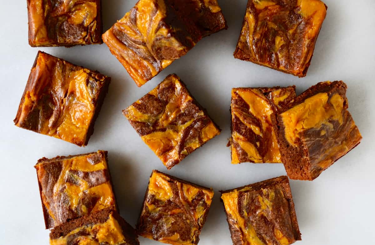 Squares of butterscotch cheesecake brownies on a white surface.