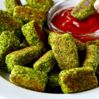 A platter of broccoli tots and a person dipping a baked broccoli tot into a small bowl of ketchup.