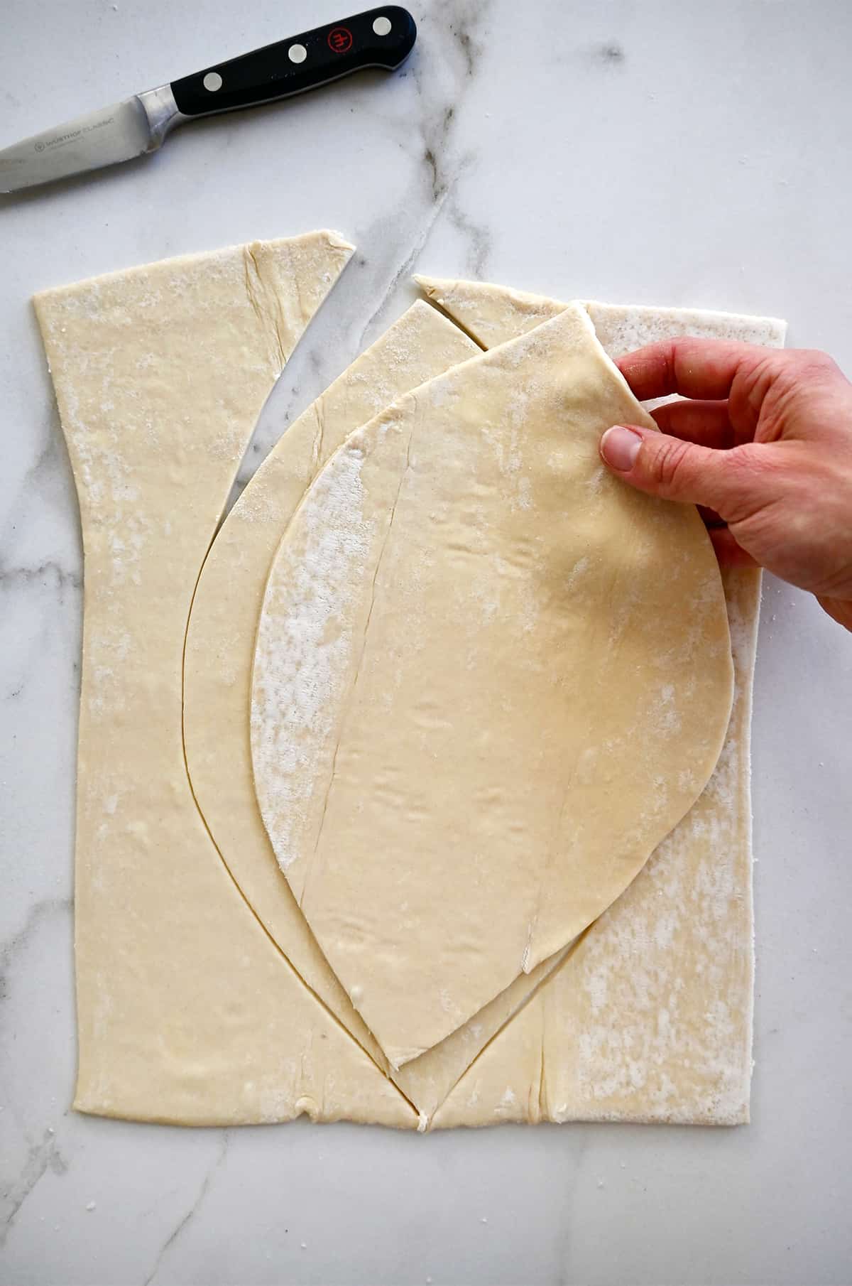 A hand holds a football-shaped piece of puff pastry over a rectangular puff pastry piece to trace.