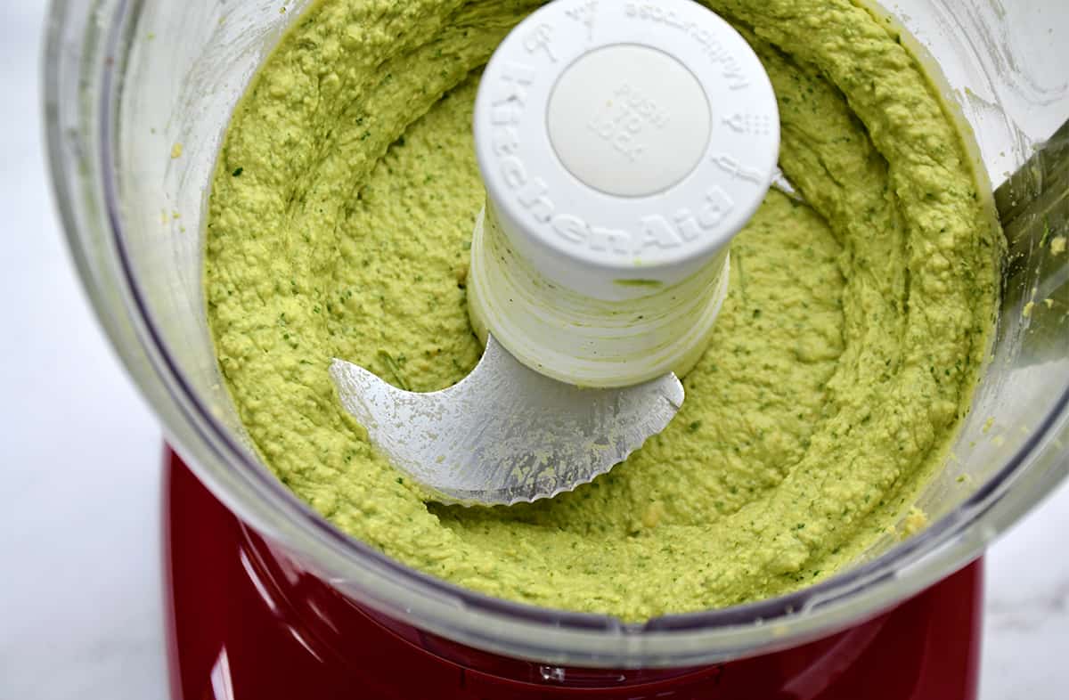 Avocado hummus in a food processor's bowl fitted with an S-blade. The food processor's lid is off.
