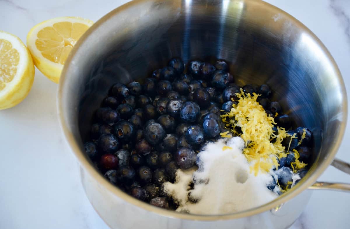 Blueberries, sugar and lemon zest in a saucepan. A halved lemon sits beside the saucepan.