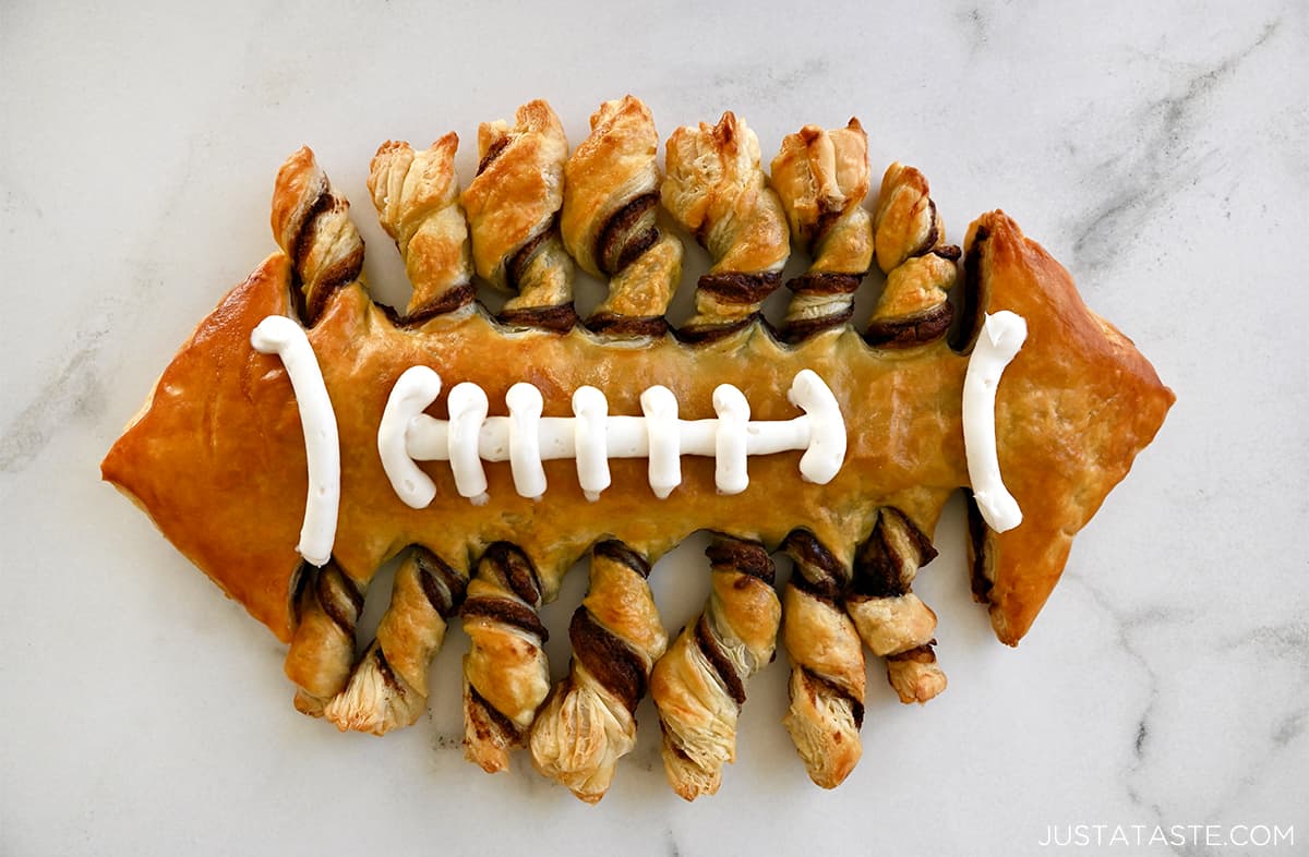 A puff pastry football with vanilla frosting laces on a marble countertop.