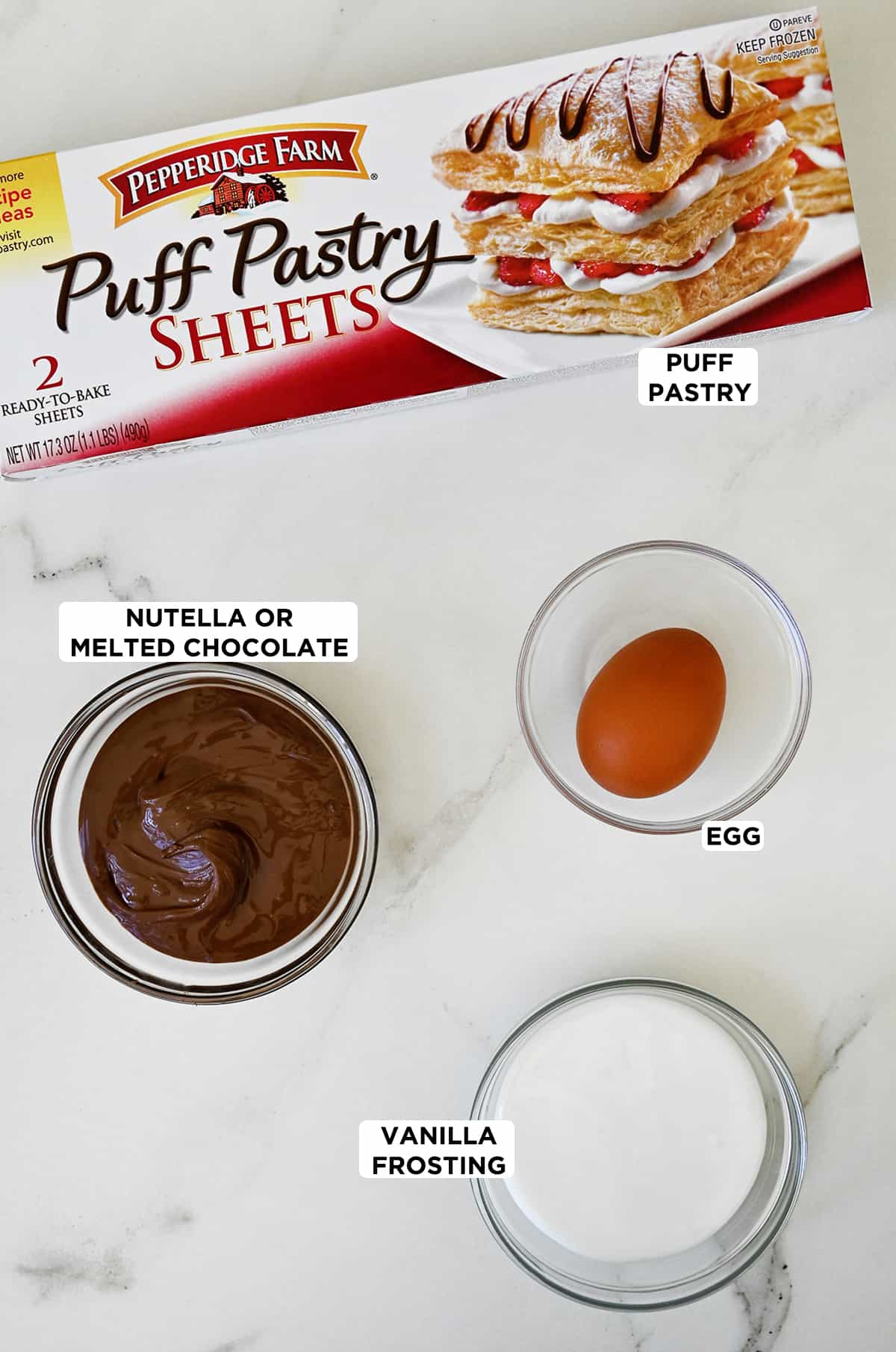 A box of puff pastry sheets next to three glass bowls containing Nutella, an egg and vanilla frosting.