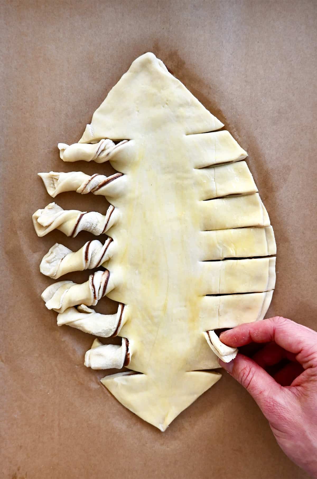 Puff pastry in the shape of a football with twisted edges on a parchment paper-lined baking sheet.