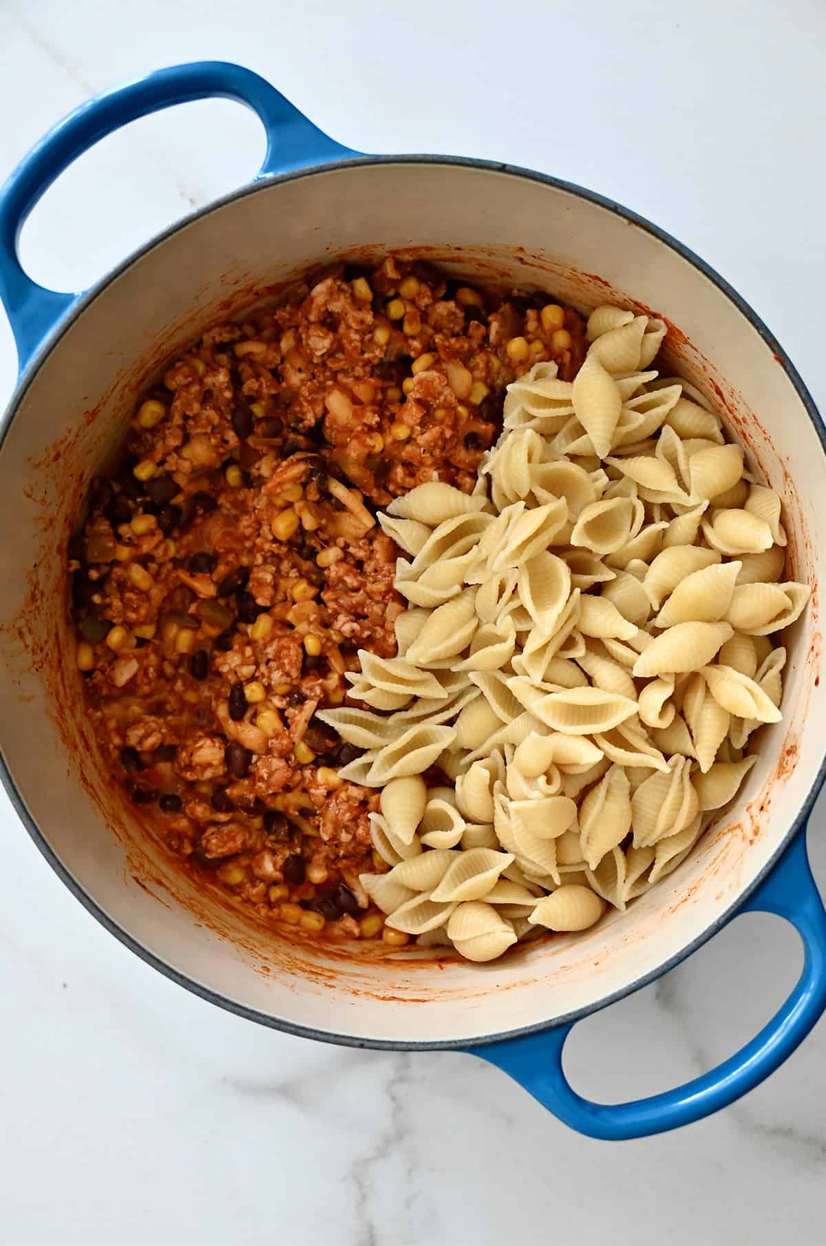 Cooked pasta shells in a Dutch oven with ground turkey taco mixture.