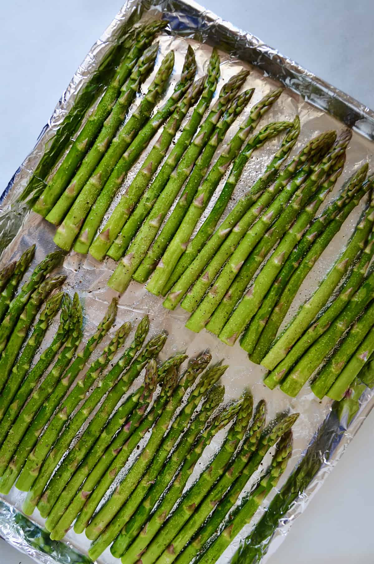 Two rows of asparagus seasoned with salt and pepper on a foil-lined baking sheet.