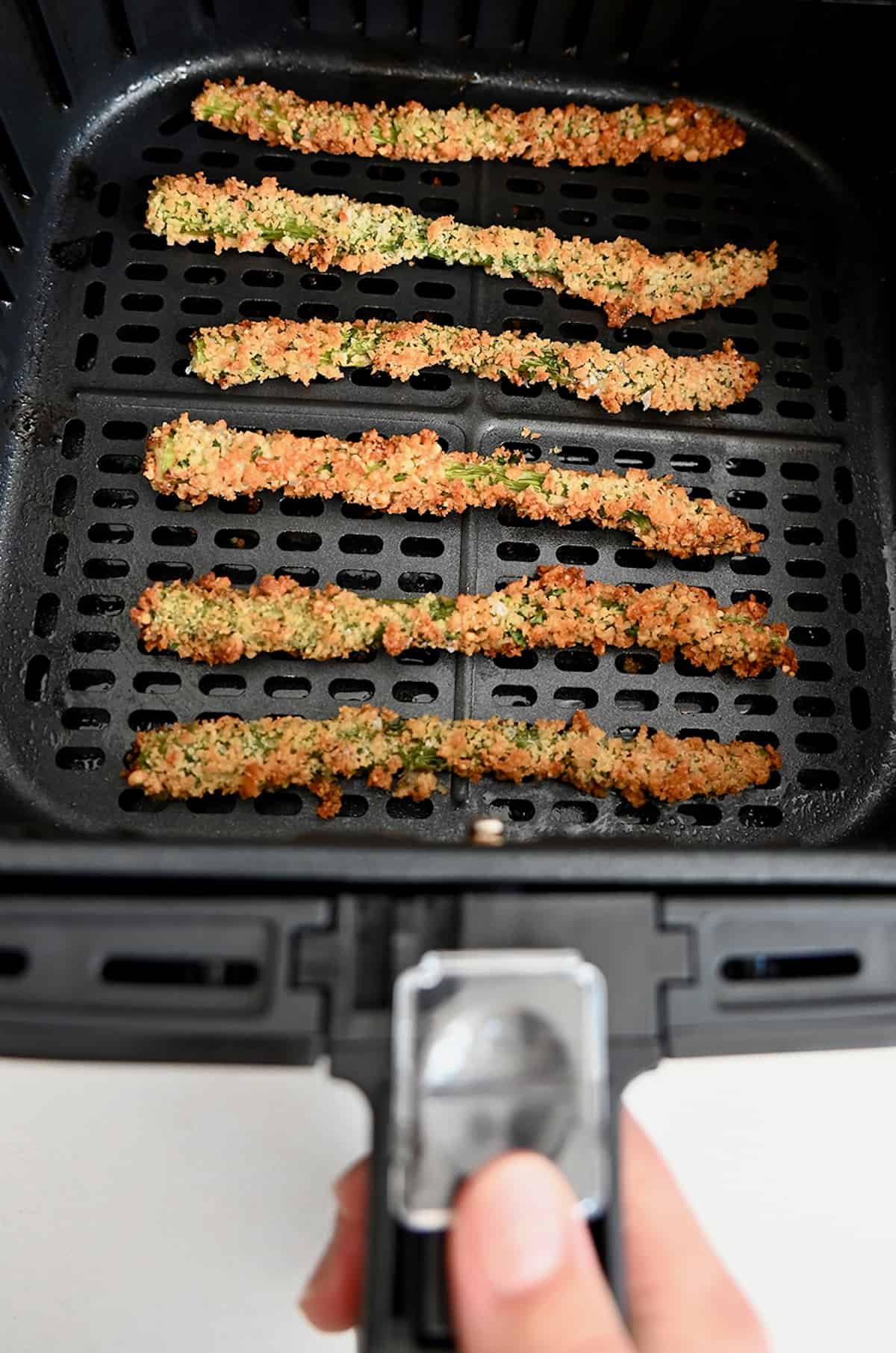 Baked asparagus fries are lined up in the basket of an air fryer.