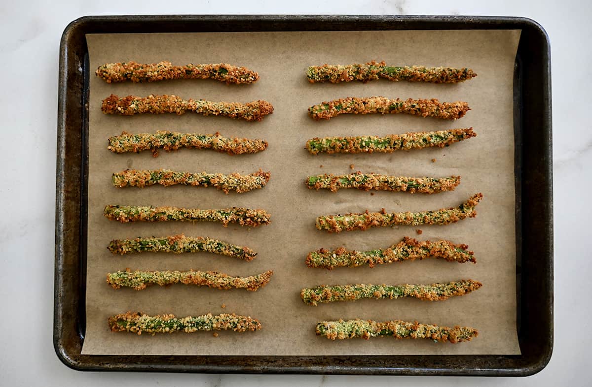 Rows of baked asparagus fries sit on a parchment-lined baking sheet.