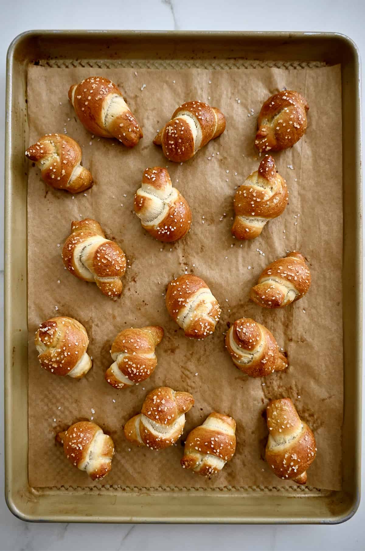 Golden brown pretzel knots on a parchment paper lined baking sheet.