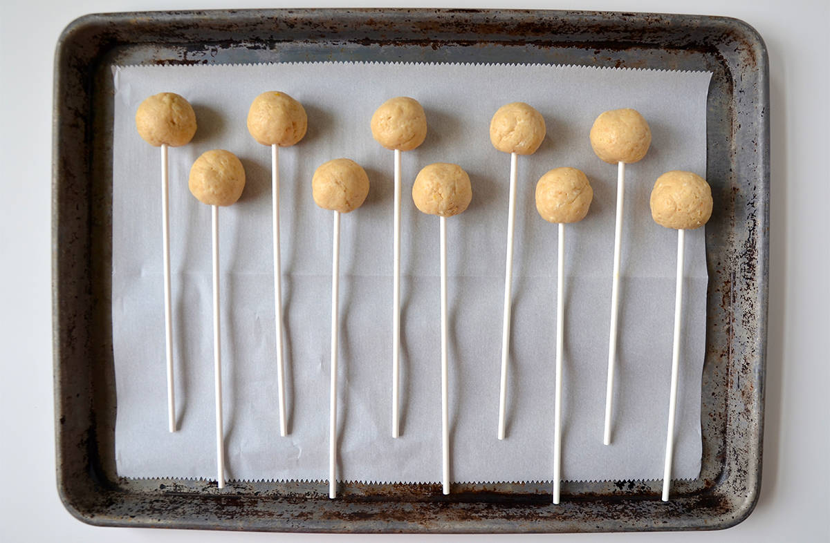 No-bake cheesecake cookie pops on a parchment-lined baking sheet.