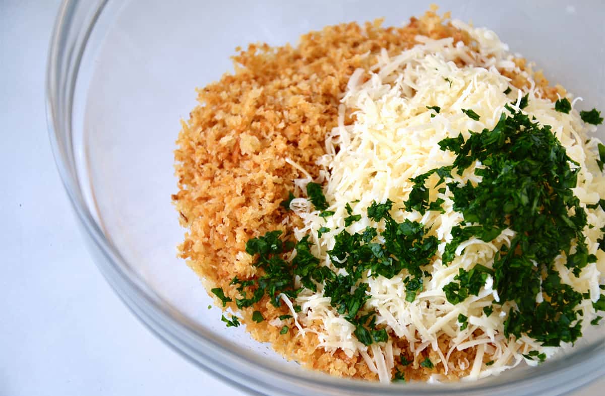 Toasted breadcrumbs, grated cheese and chopped parsley in a glass mixing bowl.