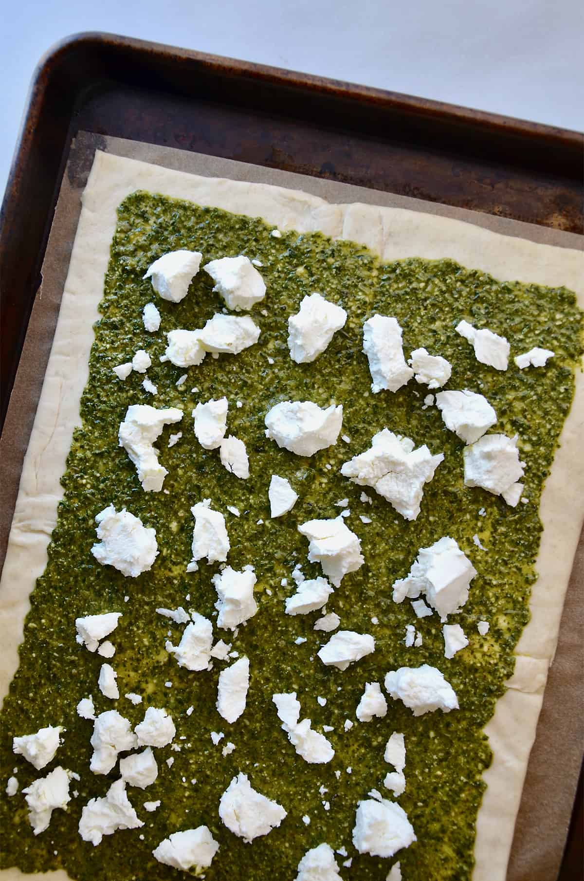 A rectangle of puff pastry topped with pesto and crumbled goat cheese.