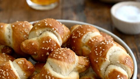 Pizza dough soft pretzel knots piled high in a white bowl with two glasses of beer nearby.