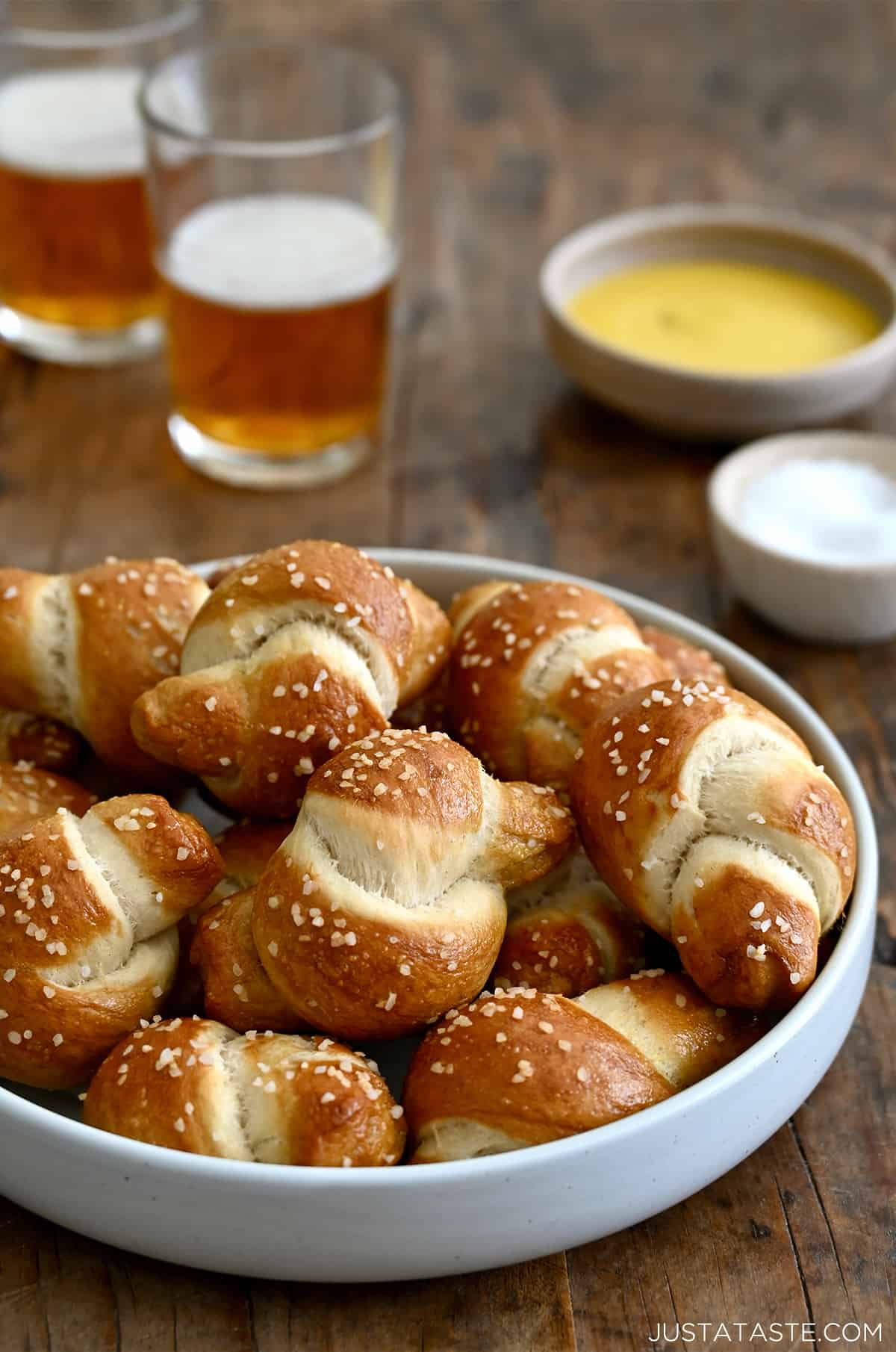 Pizza dough soft pretzel knots piled high in a white bowl with two glasses of beer nearby.