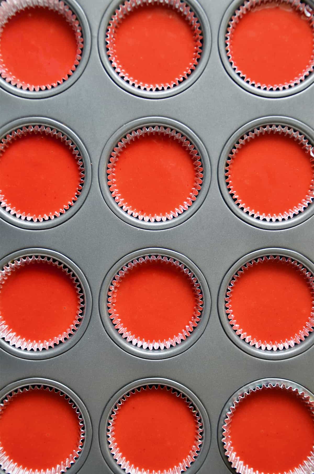 Red velvet cake batter is in cupcake papers in a cupcake tin.