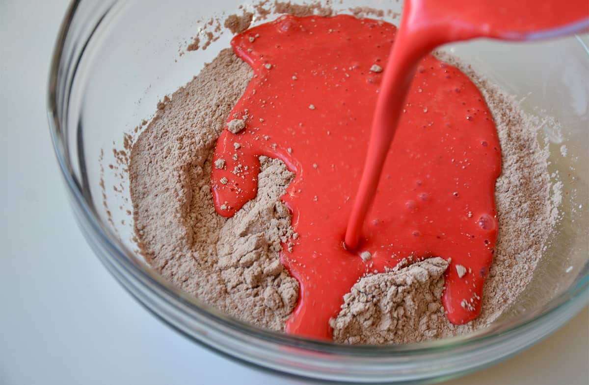 The wet ingredients are being poured into dry ingredients in a bowl to make red velvet pancake batter.