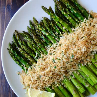 Roasted asparagus topped with cheesy, herby breadcrumbs on a white serving plate.