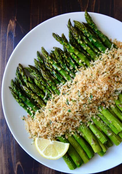 Roasted asparagus topped with cheesy, herby breadcrumbs on a white serving plate.
