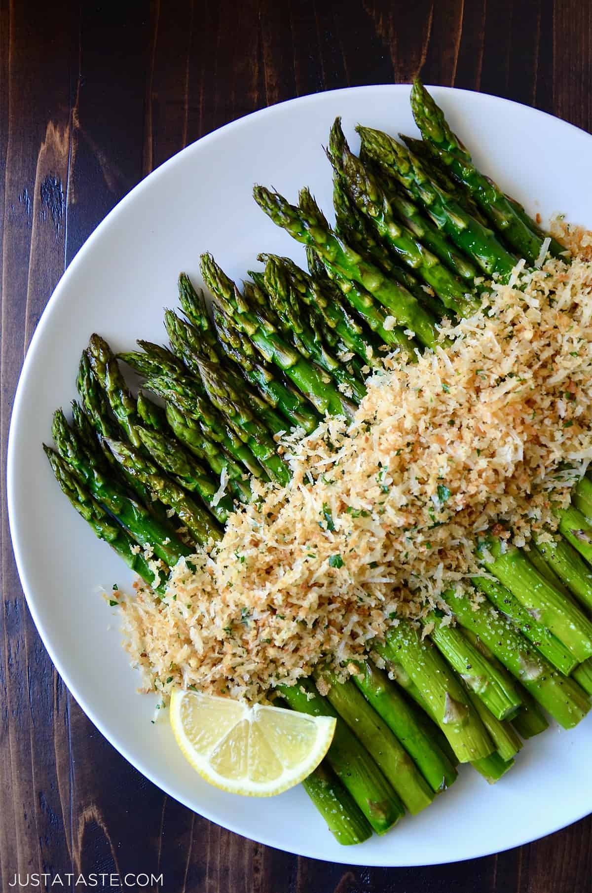 Roasted asparagus topped with cheesy, herby breadcrumbs on a white serving plate.
