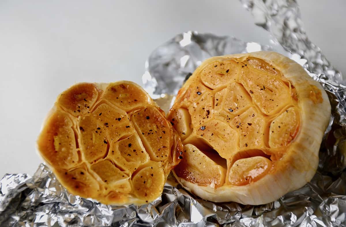 A head of roasted garlic, sliced in half, is in aluminum foil.
