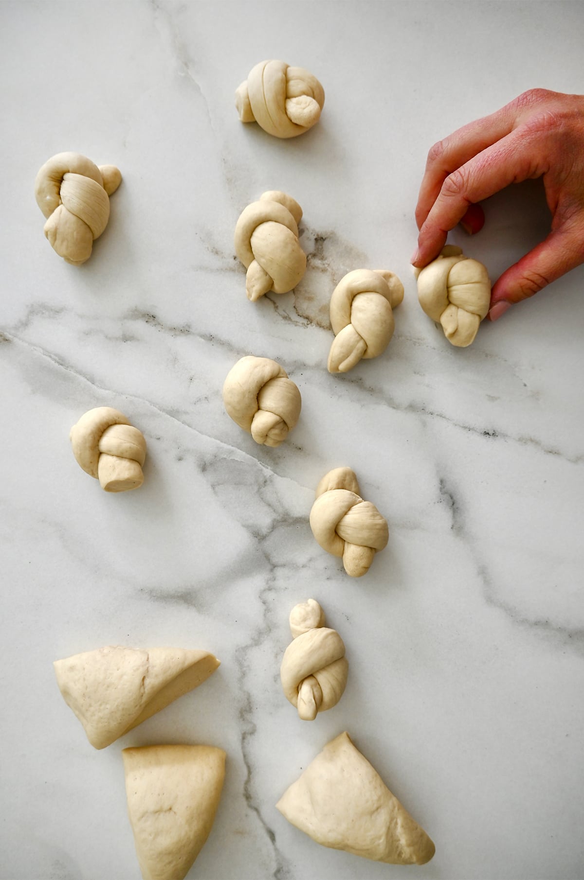 Pizza dough shaped into knots on a marble surface.