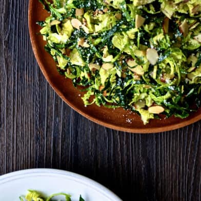 Two plates of shredded kale and Brussels sprouts salad with sliced almonds, topped with grated Parmesan cheese.