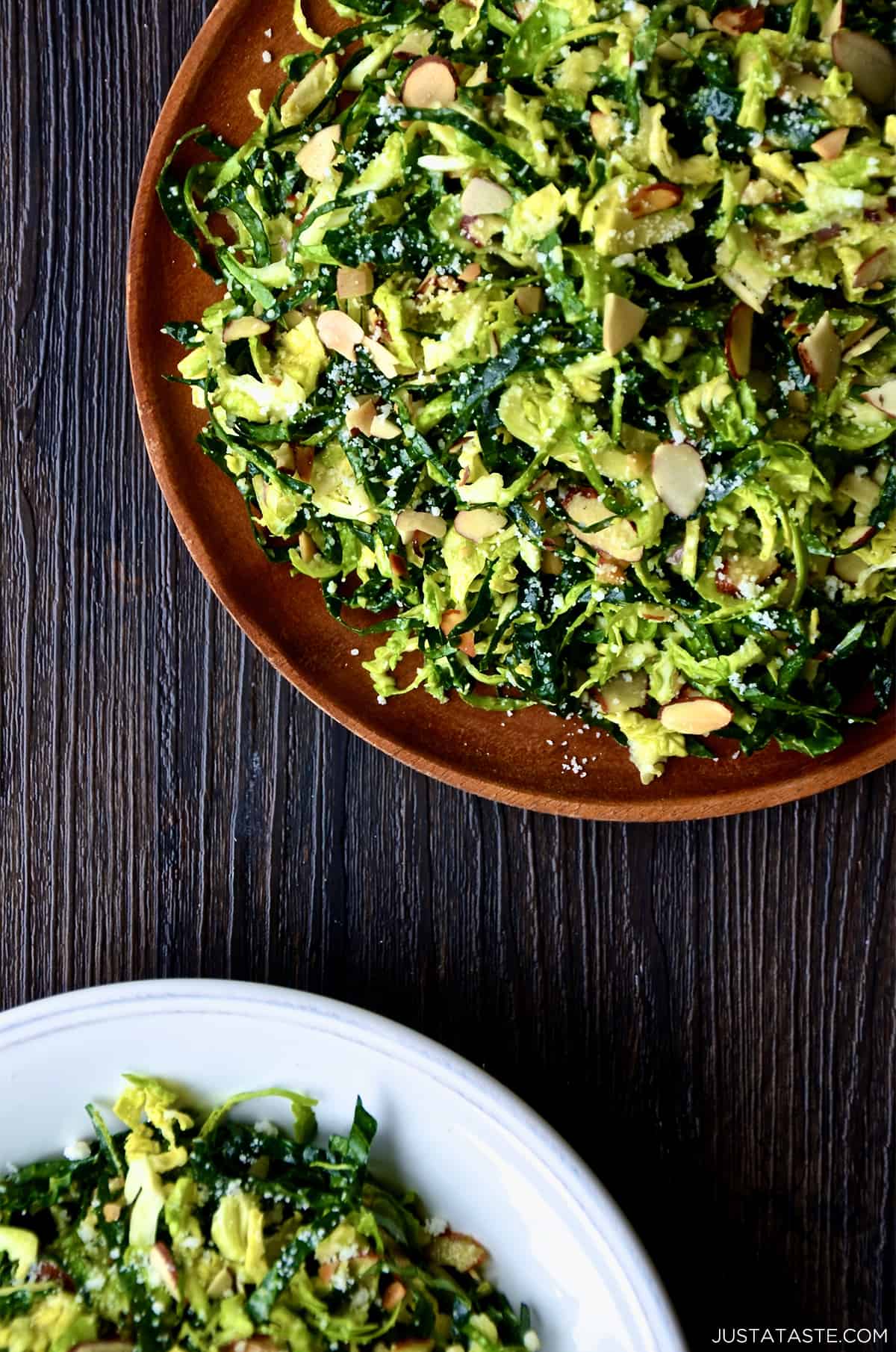 Two plates of shredded kale and Brussels sprouts salad with sliced almonds, topped with grated Parmesan cheese.